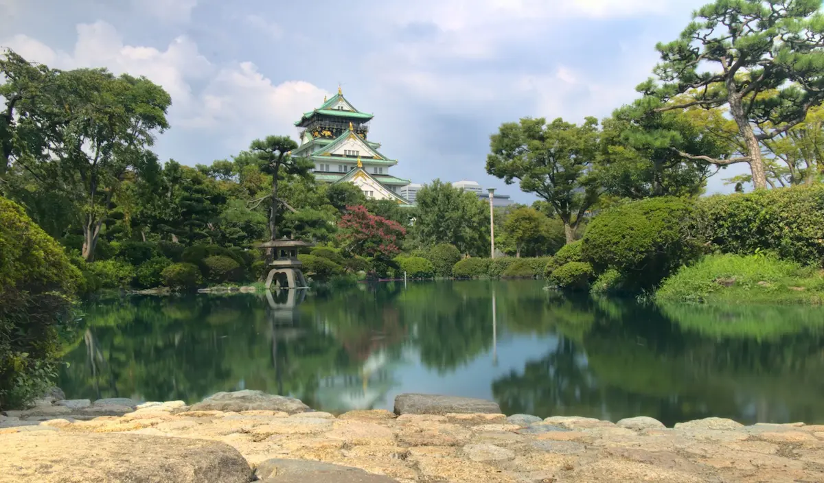 Here you can see Osaka Castle in the background. Since the camera was close to the ground you can see the cobble stone floor, behind which lies a calm small lake. This lake is surrounded by a beautiful and delicately designed japanese garden.