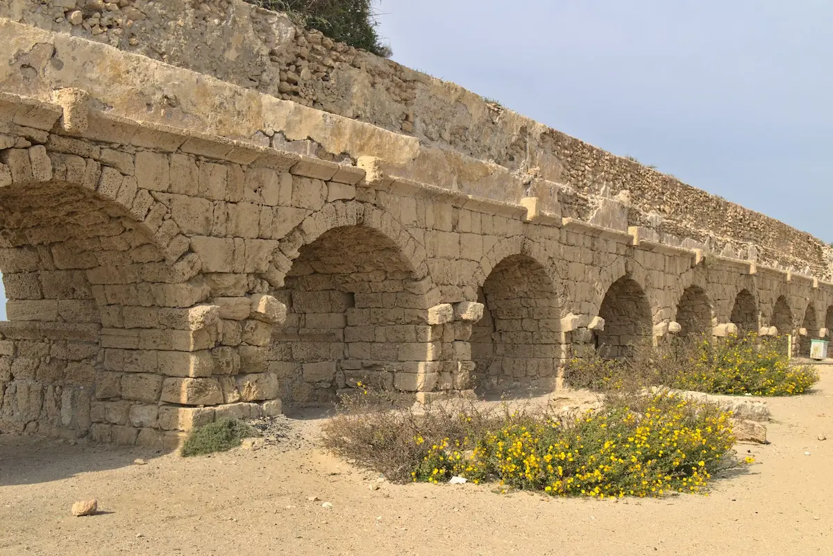 An ancient aqueduct, which has definetly seen better days is the focus of the image. The ground is made up of sand.